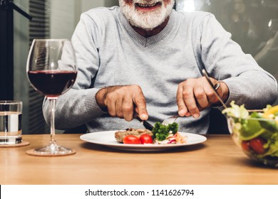 Happy Senior Man Eating Pork Steak On Table At Restaurant 