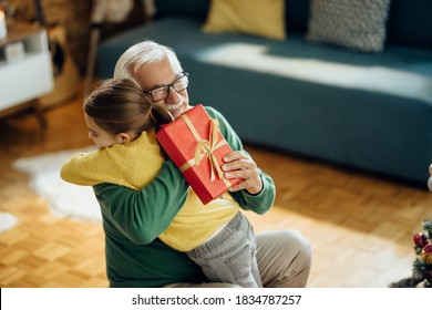 Happy senior man embracing his granddaughter while receiving a gift on Christmas at home.  - Powered by Shutterstock