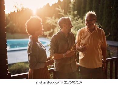 Happy Senior Man Enjoying In Conversation With His Mature Son And African American Daughter In Law While Having A Drink On Patio At Sunset.