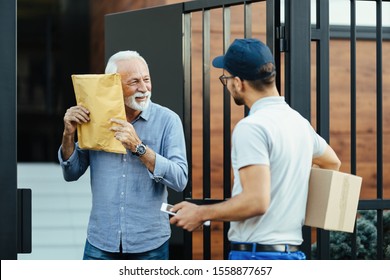 Happy Senior Man Getting A Delivery From Courier And Feeling Curious What Is Inside Of A Package. 