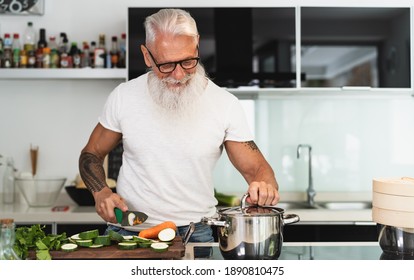 Happy senior man having fun cooking at home - Elderly person preparing health lunch in modern kitchen - Retired lifestyle time and food nutrition concept - Powered by Shutterstock