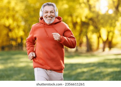 Happy senior man in headphones and sportswear jogging running outside in autumn park. Healthy active lifestyle on retirement and sport outdoor concept - Powered by Shutterstock