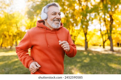 Happy senior man in headphones and sportswear jogging running outside in autumn park. Healthy active lifestyle on retirement and sport outdoor concept - Powered by Shutterstock