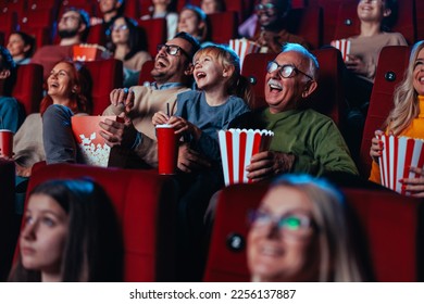 A happy senior man is with his grandchild in cinema enjoying a movie, popcorns and beverages over the weekend.