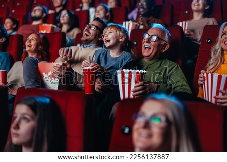 A happy senior man is with his grandchild in cinema enjoying a movie, popcorns and beverages over the weekend.