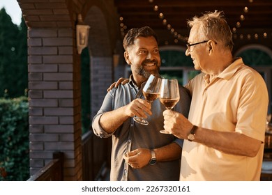 Happy senior man and his son toasting with wine during family gather on a terrace.