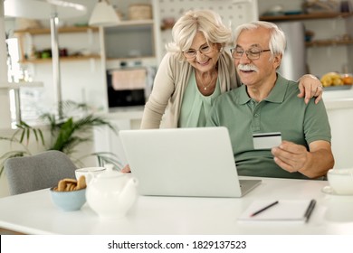 Happy Senior Man And His Wife Using Credit Card And Laptop While Online Banking At Home. 