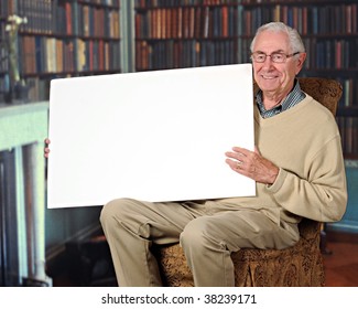 A Happy Senior Man Holding A Blank Sign In A Home Library.