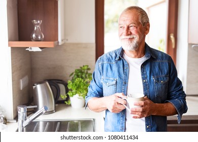 Happy senior man holding a cup of coffee in the kitchen. - Powered by Shutterstock