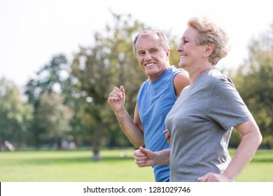 Happy senior man looking at woman while jogging in park - Shutterstock ID 1281029746