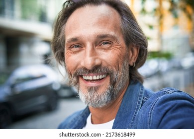 Happy Senior Man On Street Of European City Making Selfie Using Mobile Phone. Middle Aged Handsome Grey Bearded Man Smiling On Camera Old Town Wearing Casual. Travel Concept. 