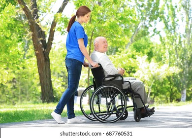 Happy Senior Man On Wheelchair With Young Female Volunteer Outdoors