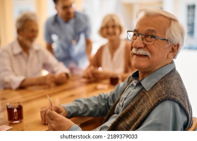 Happy senior man playing card with his friends at nursing home an looking at camera.  - Powered by Shutterstock