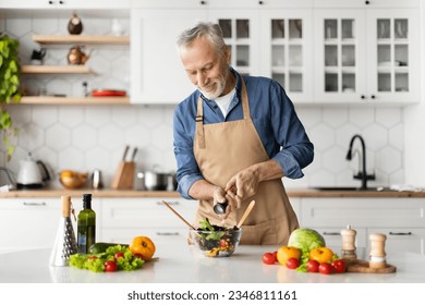 Happy senior man preparing healthy vegetable salad in kitchen, seasoning meal, smiling elderly gentleman in apron adding salt to bowl, enjoying cooking vegetarian food at home, free space - Powered by Shutterstock