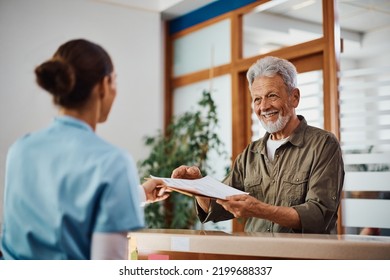 Happy senior man receiving his medical documents from nurse at reception desk at doctor's office. - Powered by Shutterstock