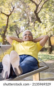 Happy senior man relaxing with hands behind head and feet up at park bench