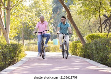 Happy Senior Man Riding Bicycle With His Young Son At Park
