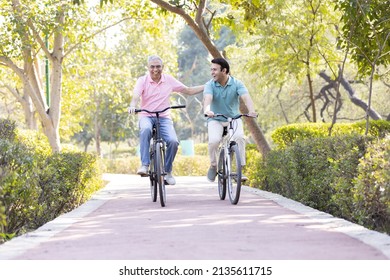 Happy Senior Man Riding Bicycle With His Young Son At Park
