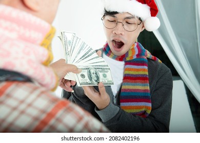 Happy Senior Man With Scarf And Santa Hat Give Money To His Son For Celebrate Christmas Eve On White Background. Dollar Bills That A Father Gives His Son For Save In Special Day. 