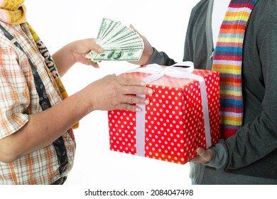 Happy Senior Man With Scarf And Santa Hat Give Money Or Dollar Bills To His Son, While His Son Give Giftbox For His Father For Celebrate Christmas Eve And Happy New Year On White Background.