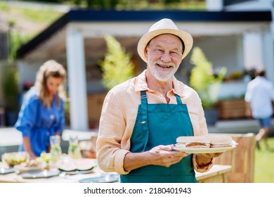 Happy senior man serving burgers at multi generation garden party in summer. - Powered by Shutterstock