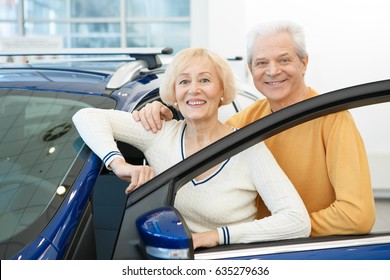 Happy Senior Man Smiling Joyfully Embracing His Cheerful Wife Standing Together Near His Newly Bought Automobile At The Dealership Insurance Safety Driving Retirement Ownership Travelling Transport