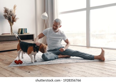 Happy senior man in sport clothing exercising at home near his dog 