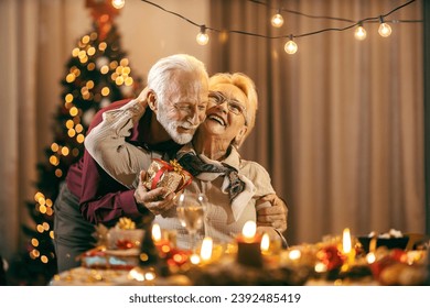 A happy senior man is surprising his wife with christmas present on christmas and new year's eve at home while she is hugging him. - Powered by Shutterstock