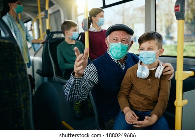 Happy Senior Man Talking To His Grandson While Commuting By Bus And Wearing Face Masks Dur To COVID-19 Pandemic.