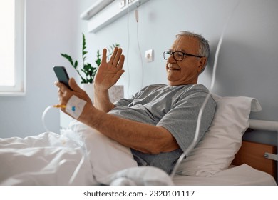 Happy senior man using cell phone and waving during video call while recovering in the hospital.  - Powered by Shutterstock