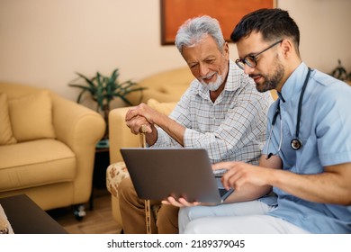 Happy Senior Man Using Laptop With Help Of Male Caregiver During Home Visit. 