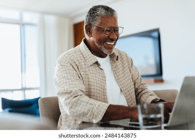 Happy senior man using a laptop at home, enjoying technology and staying connected. - Powered by Shutterstock