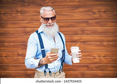 Happy Senior Man Using Smartphone App Outdoor With Wood Background - Fashion Old Guy Having Fun With New App Trend Technology - Tech And Joyful Elderly Lifestyle Concept - Focus On His Face