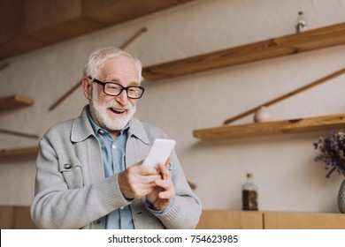 Happy Senior Man Using Smartphone And Looking At Camera