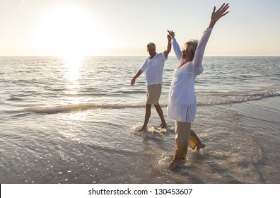 Happy senior man and woman couple dancing and holding hands on a deserted tropical beach at sunrise or sunset