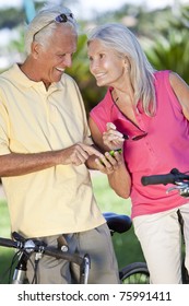 Happy Senior Man And Woman Couple Cycling And Together Using A Smart Phone Outside In Sunshine