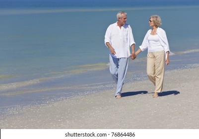 Happy senior man and woman couple together holding hands and walking on a deserted tropical beach