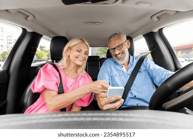 Happy senior man and woman having car trip together, using cell phone and smiling, copy space. Cheerful elderly couple travellers enjoying journey by cozy auto, tracking their way on smartphone - Powered by Shutterstock