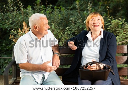 Happy senior man and woman having conversation on bench in green park