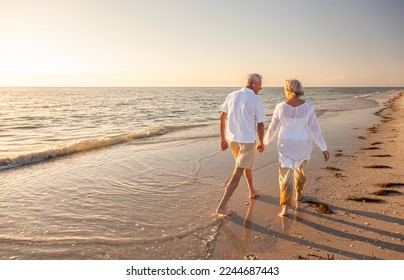 Happy senior man and woman old retired couple walking and holding hands on a beach at sunset, s3niorlife