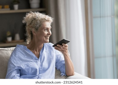 Happy senior mature lady talking on speaker on cellphone call, speaking at dynamic, holding smartphone at face, recording audio message, resting at home, smiling, laughing, enjoying communication - Powered by Shutterstock