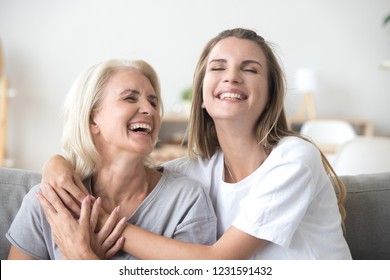 Happy senior mature mother embracing young adult woman laughing together, smiling elderly older mum joking having fun with grown daughter, two age generations humor and positive emotions concept