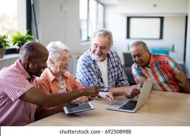 Happy senior men and woman using laptop while sitting at table in nursing home - Powered by Shutterstock