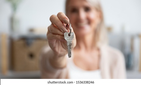 Happy senior middle aged woman customer landlord hold key to new house apartment give to camera, older retired female hand real estate owner make sale purchase property deal concept, close up view