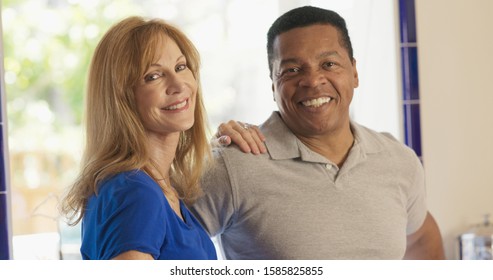 Happy Senior Mixed Race Couple Homeowners Looking At Camera. Older Caucasian And African American Husband And Wife Standing In Their Kitchen Smiling