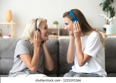 Happy senior mother and adult daughter laughing listening to music in wireless earphones together, smiling young old women wearing headphones having fun enjoy favorite song relaxing at home