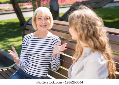 Happy Senior Mother And Daughter Sitting On Park Bench And Talking