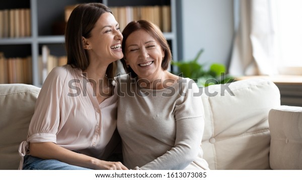 Happy senior mother and grownup daughter sit\
relax on couch in living room talk laugh and joke, smiling\
overjoyed middle-aged mom and adult girl child rest at home have\
fun enjoying weekend\
together