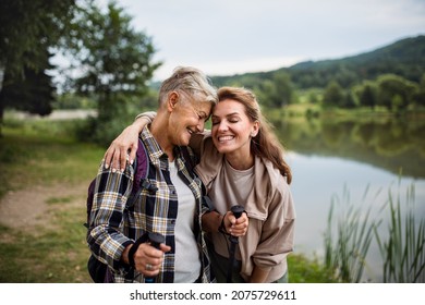 Happy Senior Mother Hiker Embracing With Adult Daughter By Lake Outdoors In Nature