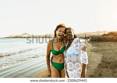 Happy senior multiracial women having fun on the beach during summer holidays - Diverse elderly friends enjoying vacations 